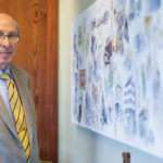 Founder Fred J. Reinders in grey and blue suit next standing in front of a wood door.